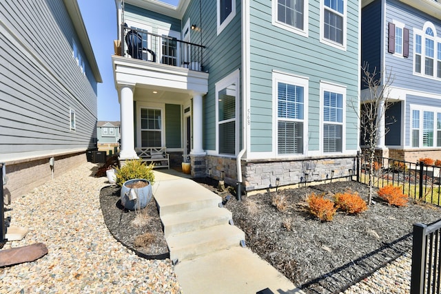 property entrance with a porch, a balcony, fence, and stone siding