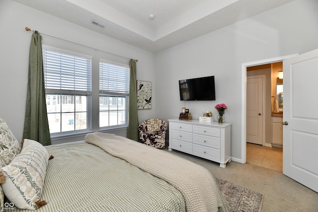 bedroom with a tray ceiling, light tile patterned floors, visible vents, and light carpet