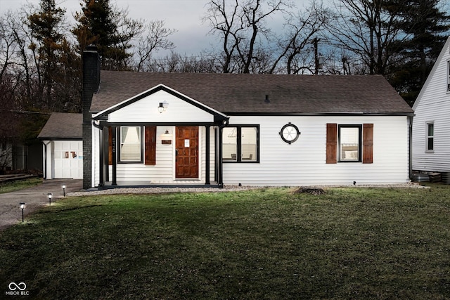 view of front of property with a shingled roof, a front yard, a chimney, driveway, and an attached garage