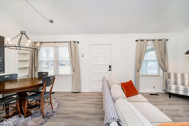 living room featuring baseboards, lofted ceiling, an inviting chandelier, and light wood-style flooring