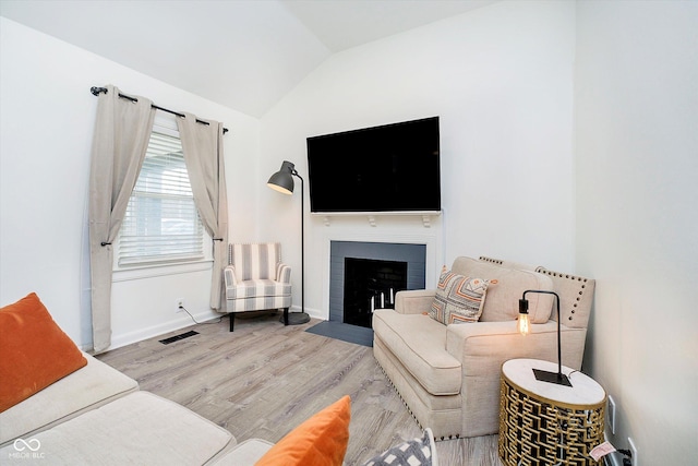 living room featuring visible vents, baseboards, a fireplace with flush hearth, lofted ceiling, and wood finished floors