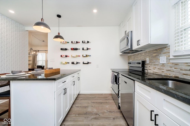 kitchen with dark stone countertops, light wood-type flooring, white cabinets, appliances with stainless steel finishes, and tasteful backsplash