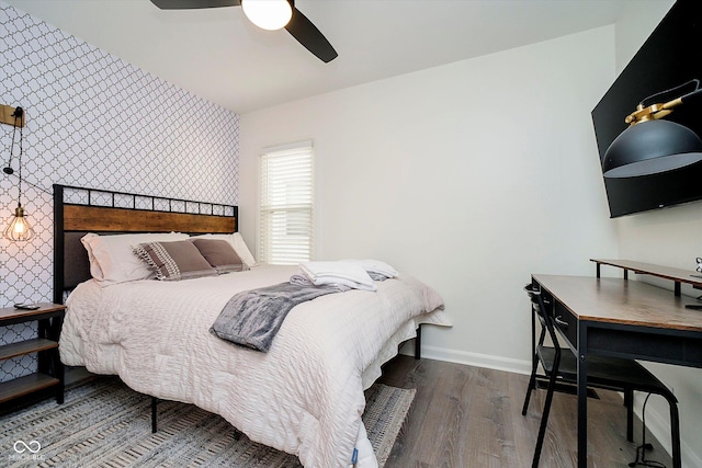 bedroom with wood finished floors, baseboards, wallpapered walls, ceiling fan, and an accent wall