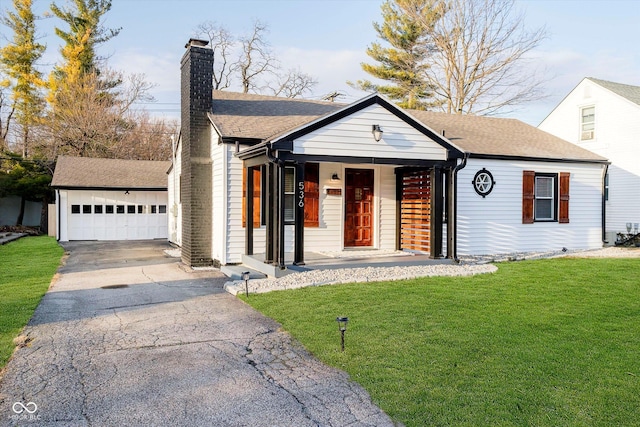 view of front of house featuring a shingled roof, a front yard, a detached garage, and a chimney