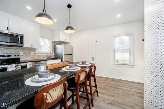 kitchen featuring light wood-style flooring, stainless steel appliances, decorative backsplash, hanging light fixtures, and a kitchen bar