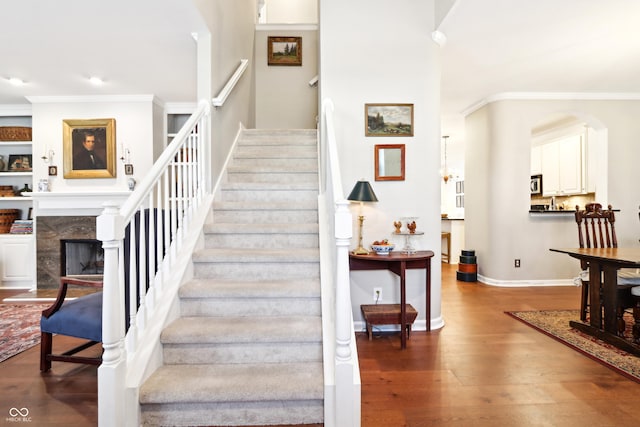 stairway with a high end fireplace, baseboards, ornamental molding, a towering ceiling, and wood finished floors