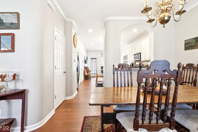 dining area with baseboards, light wood finished floors, arched walkways, ornamental molding, and a chandelier