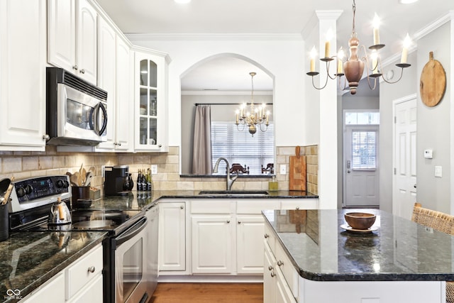 kitchen featuring ornamental molding, a sink, stainless steel appliances, glass insert cabinets, and a chandelier