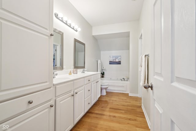 bathroom featuring a bath, double vanity, wood finished floors, and a sink