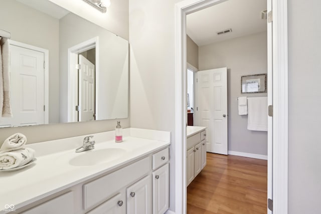 bathroom with visible vents, vanity, baseboards, and wood finished floors