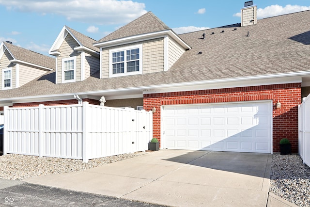 view of front of home with fence, driveway, an attached garage, a shingled roof, and brick siding