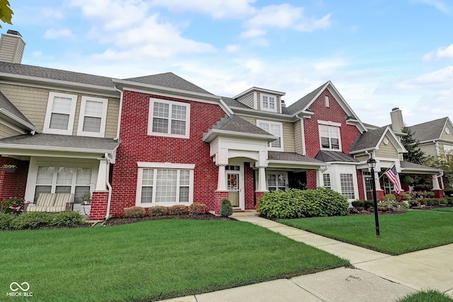 view of front of property with a chimney, brick siding, roof with shingles, and a front lawn