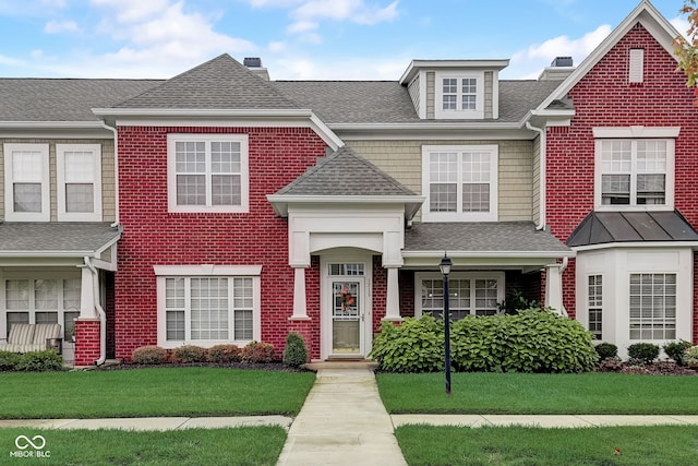 townhome / multi-family property with roof with shingles and a front lawn