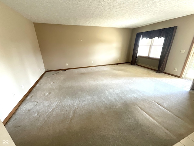 spare room with light colored carpet, baseboards, and a textured ceiling