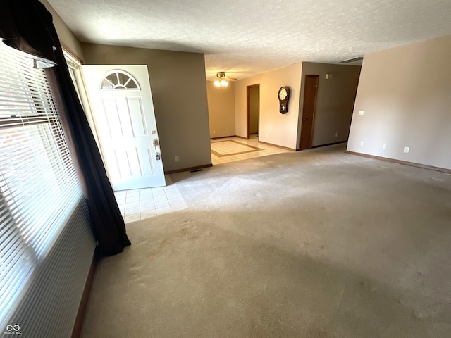 spare room featuring a ceiling fan, light colored carpet, baseboards, and a textured ceiling