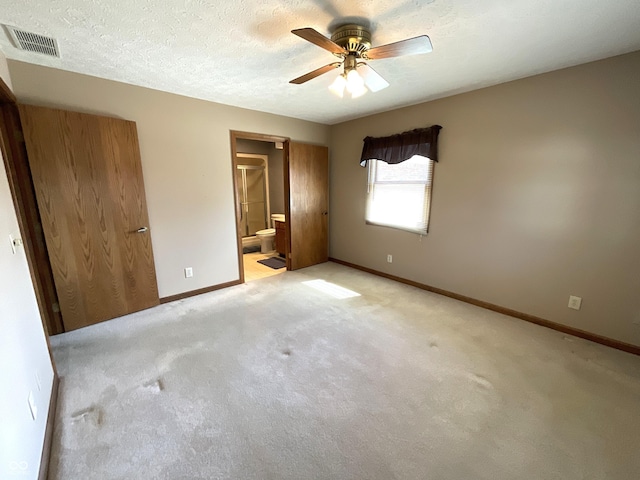 unfurnished bedroom with baseboards, visible vents, ensuite bath, a textured ceiling, and light colored carpet