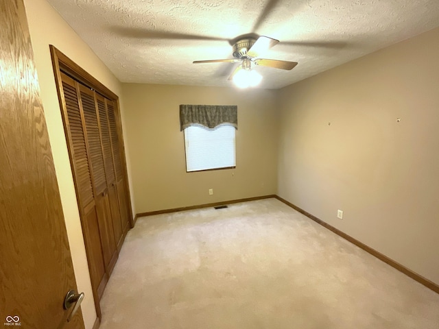 unfurnished bedroom featuring baseboards, ceiling fan, a closet, a textured ceiling, and light carpet