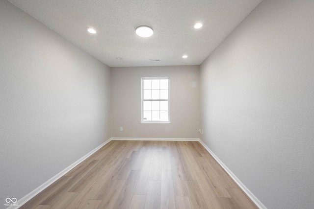 empty room with visible vents, baseboards, a textured ceiling, and light wood finished floors