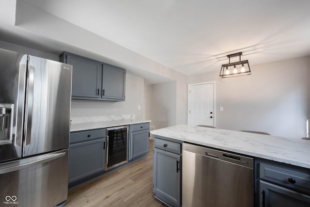 kitchen featuring light wood finished floors, gray cabinetry, beverage cooler, light stone counters, and appliances with stainless steel finishes