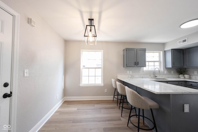 kitchen featuring light wood-type flooring, gray cabinets, a sink, a breakfast bar area, and baseboards