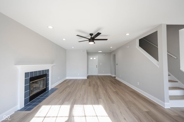 unfurnished living room featuring stairway, baseboards, light wood-style floors, and a tile fireplace