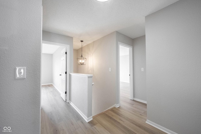 hall featuring an upstairs landing, a notable chandelier, a textured ceiling, wood finished floors, and baseboards