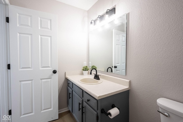 bathroom with vanity, wood finished floors, toilet, and a textured wall