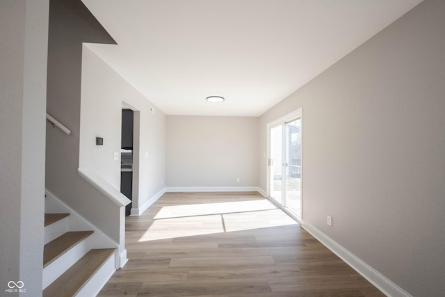 unfurnished room with stairs, light wood-style floors, and baseboards