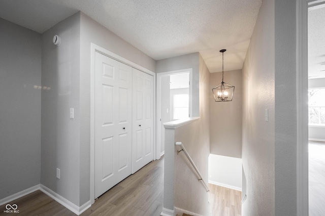 hall with an upstairs landing, a textured ceiling, wood finished floors, an inviting chandelier, and baseboards