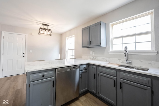 kitchen with gray cabinetry, a peninsula, stainless steel dishwasher, plenty of natural light, and a sink