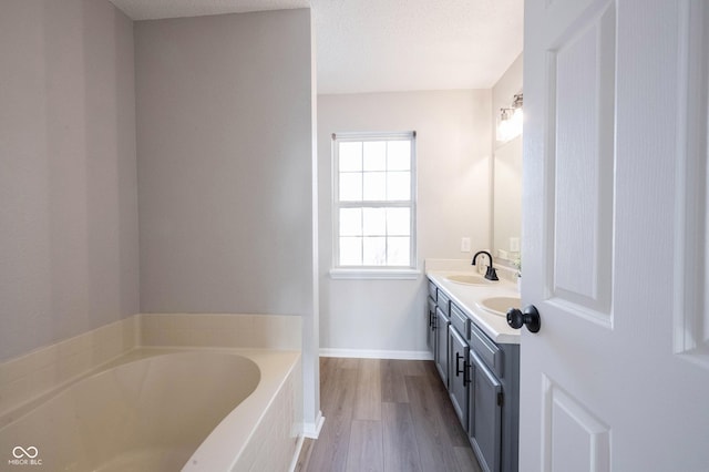 bathroom featuring a garden tub, double vanity, wood finished floors, a textured ceiling, and a sink