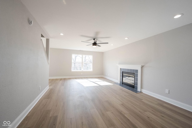 unfurnished living room with wood finished floors, baseboards, a ceiling fan, recessed lighting, and a tiled fireplace