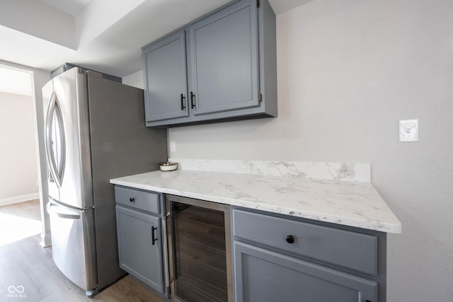 kitchen with light stone counters, light wood finished floors, freestanding refrigerator, gray cabinetry, and wine cooler