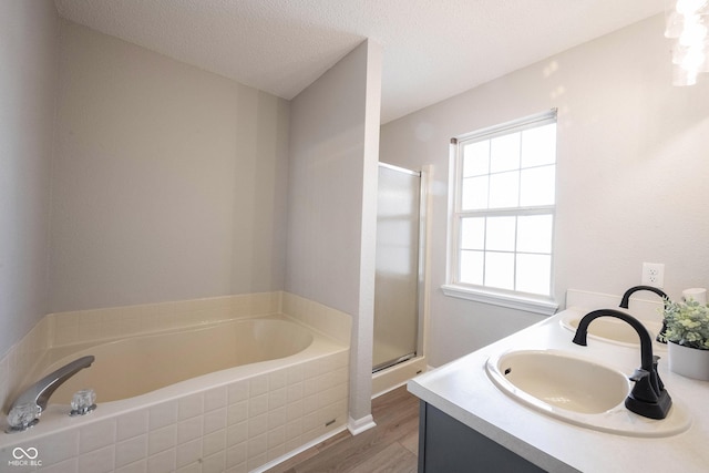 full bath with a bath, a stall shower, a textured ceiling, and a sink