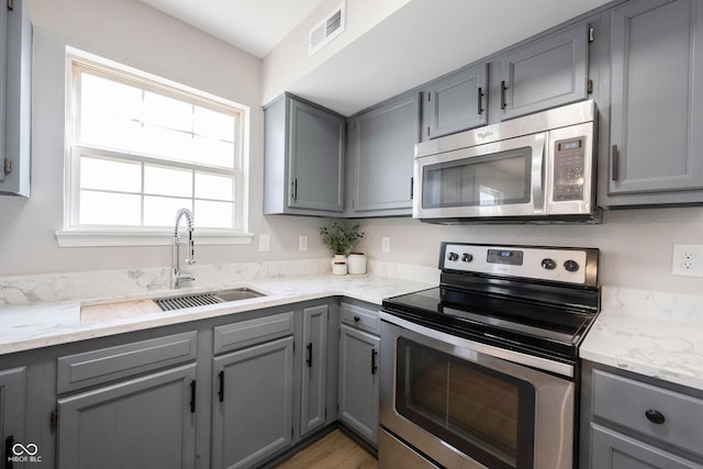 kitchen with visible vents, gray cabinetry, a sink, appliances with stainless steel finishes, and light stone countertops