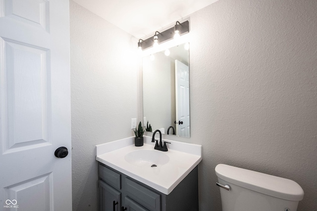 half bath featuring toilet, vanity, and a textured wall