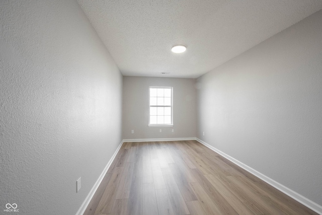 unfurnished room with a textured wall, a textured ceiling, baseboards, and wood finished floors