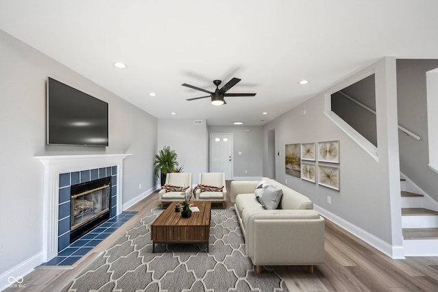 living room featuring stairway, wood finished floors, baseboards, and a tile fireplace