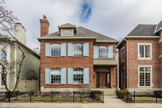 view of front facade featuring a balcony, brick siding, and a fenced front yard