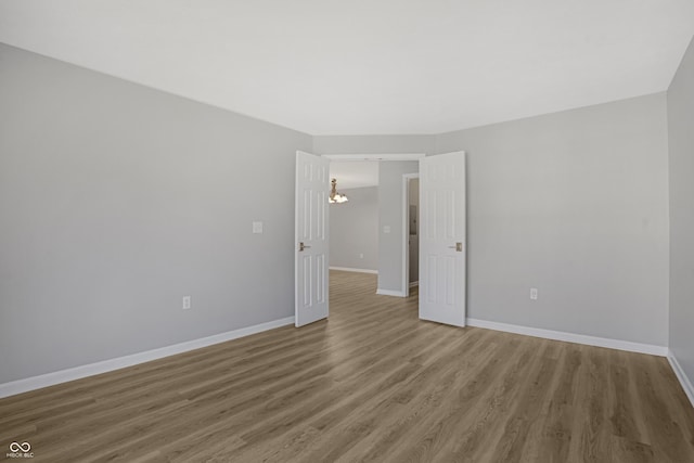 empty room featuring baseboards, an inviting chandelier, and wood finished floors