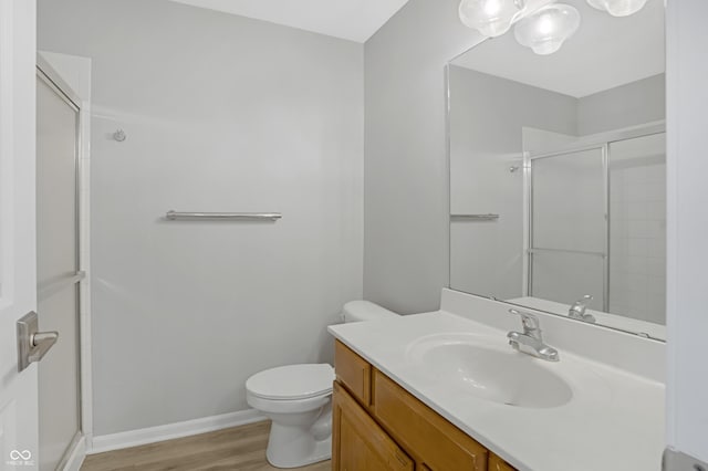 bathroom featuring vanity, wood finished floors, a shower with shower door, baseboards, and toilet