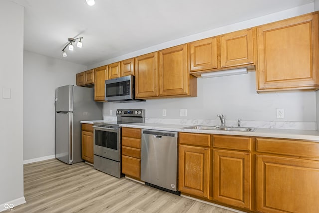 kitchen with a sink, light wood-type flooring, appliances with stainless steel finishes, and light countertops