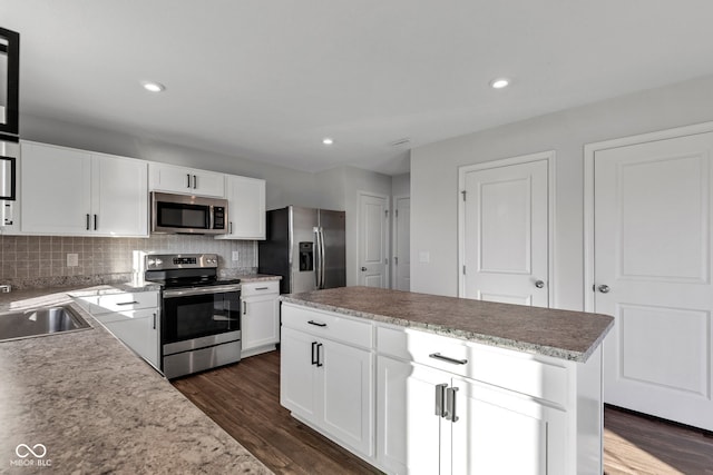 kitchen featuring a sink, a kitchen island, tasteful backsplash, appliances with stainless steel finishes, and dark wood-style flooring