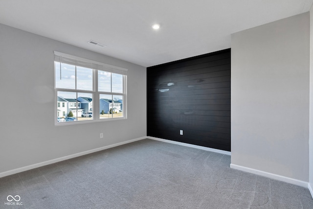 unfurnished room with visible vents, carpet floors, wood walls, baseboards, and an accent wall