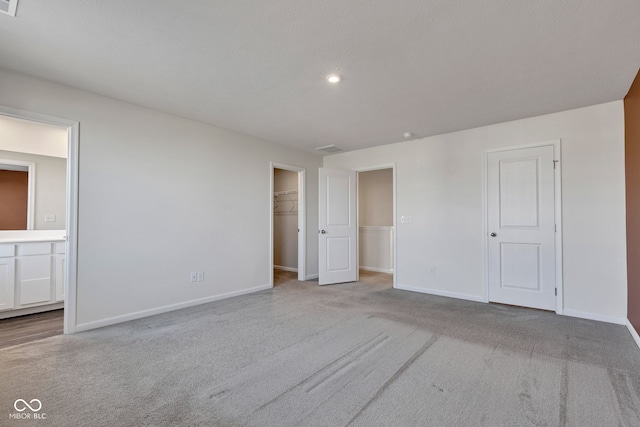 unfurnished bedroom with a spacious closet, ensuite bathroom, baseboards, and carpet floors