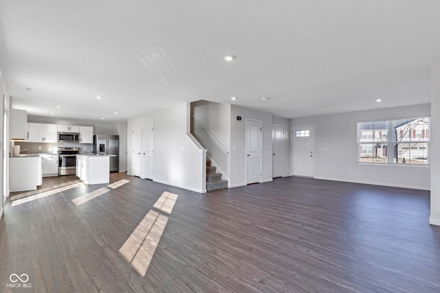 unfurnished living room with recessed lighting, baseboards, dark wood-style flooring, and stairs