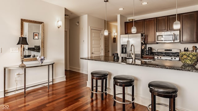 kitchen with a sink, dark brown cabinets, appliances with stainless steel finishes, a kitchen breakfast bar, and dark wood-style flooring