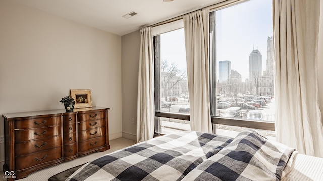 carpeted bedroom with a wall of windows, a view of city, baseboards, and visible vents