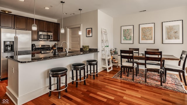 kitchen with dark brown cabinets, dark stone countertops, appliances with stainless steel finishes, dark wood-style floors, and a sink