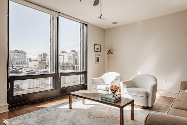 living area with visible vents, a view of city, wood finished floors, baseboards, and ceiling fan